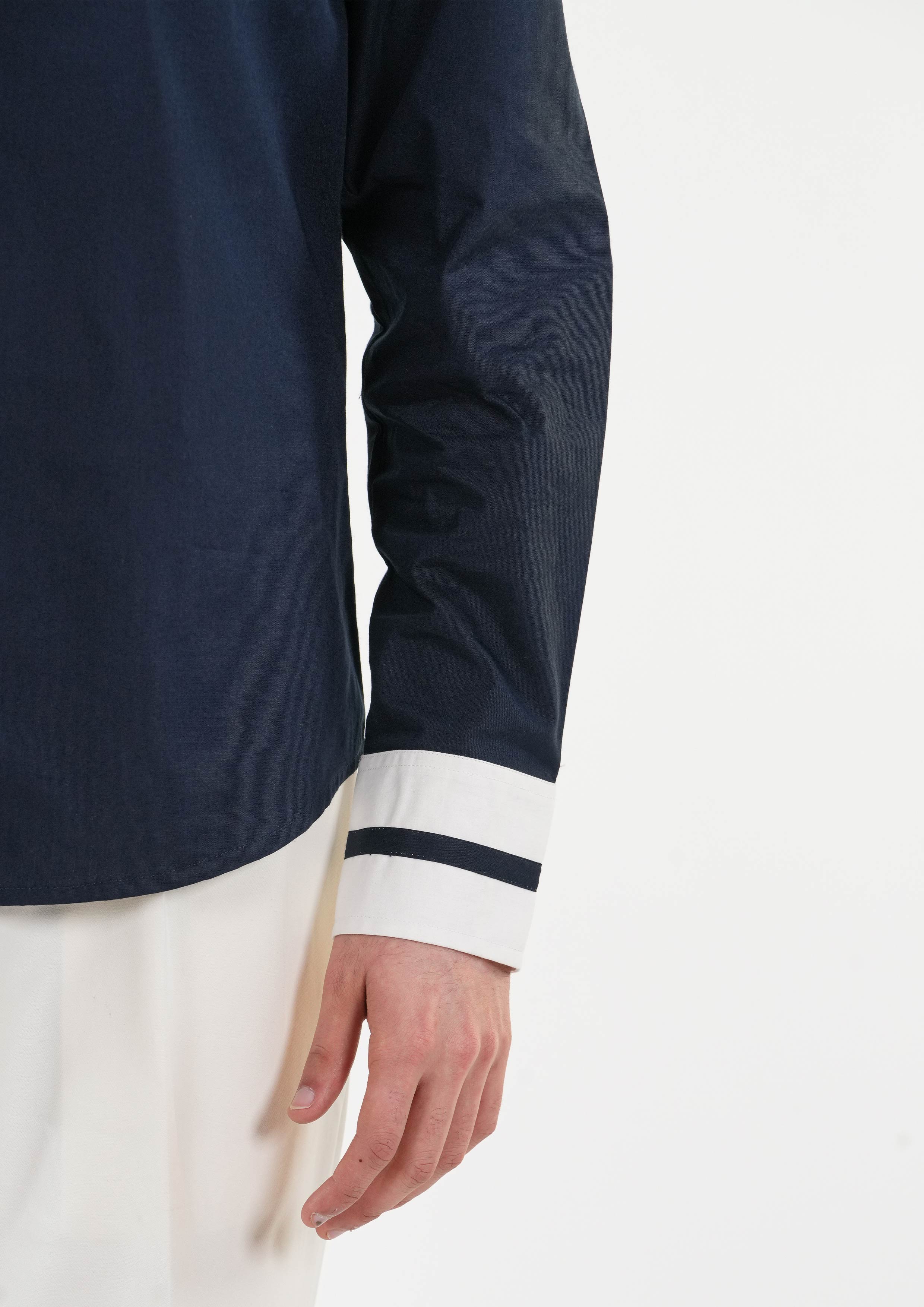Close-up of a navy long-sleeve shirt with white cuffs on a light gray background